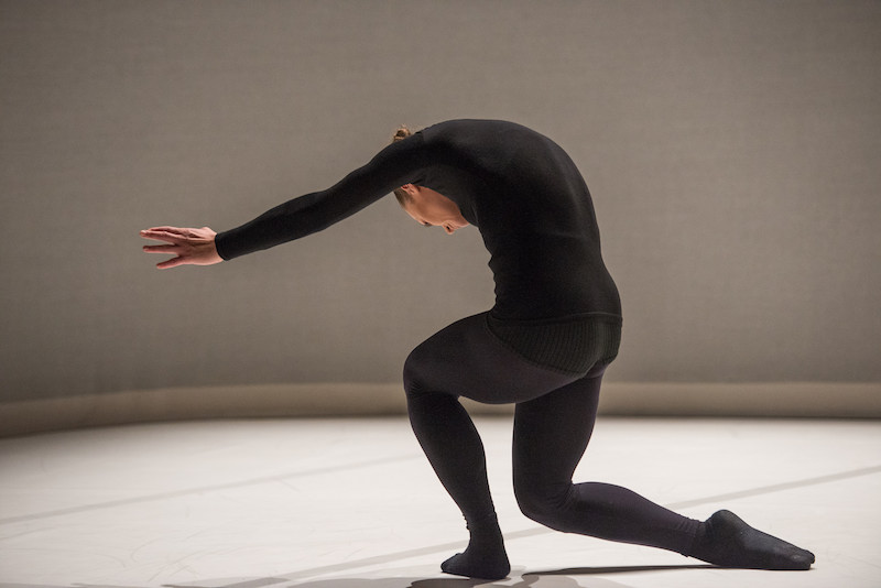 A dancer in all black curves her back over and her arms are outstreched